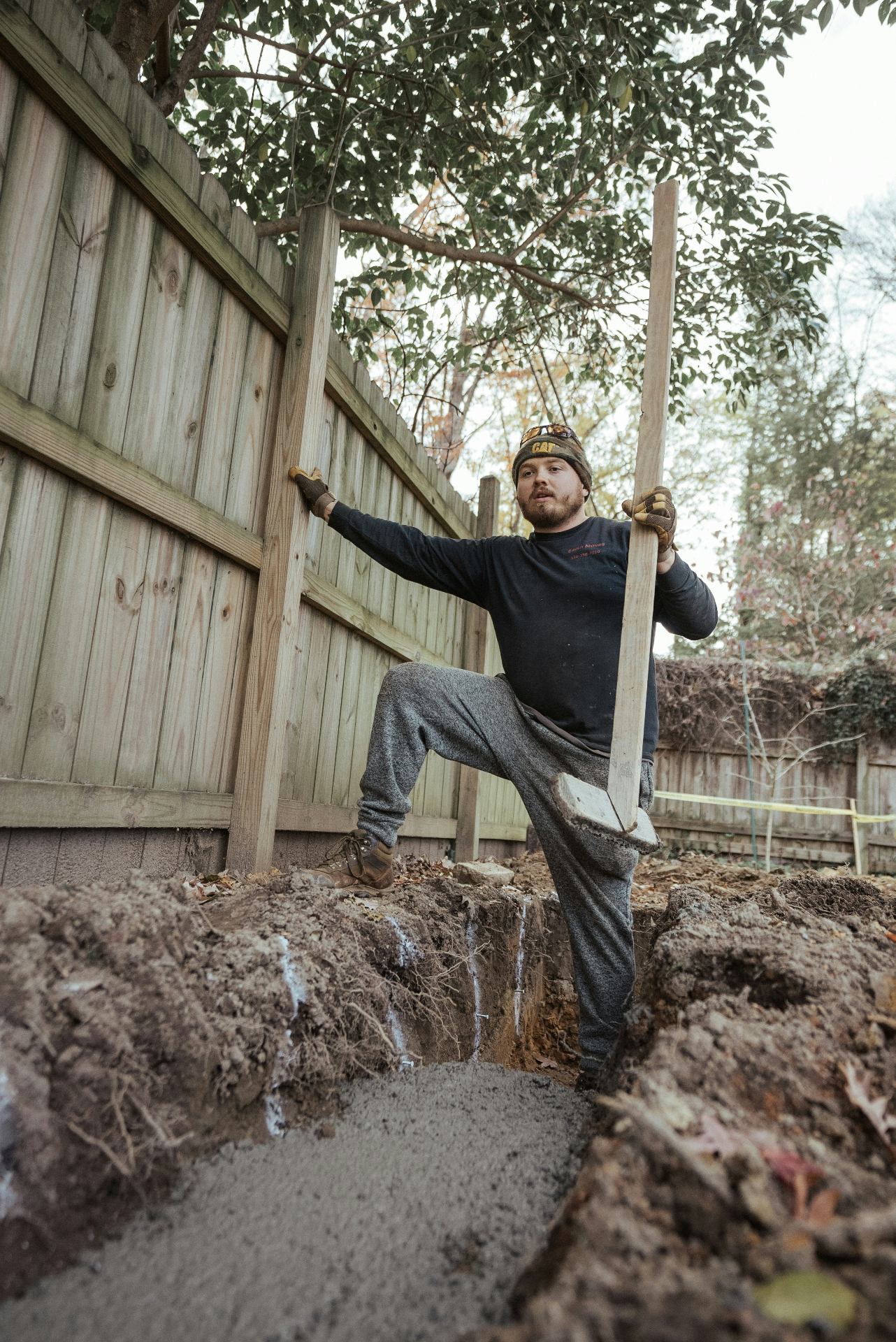 Worker standing in a trench next to fresh concrete and fence posts